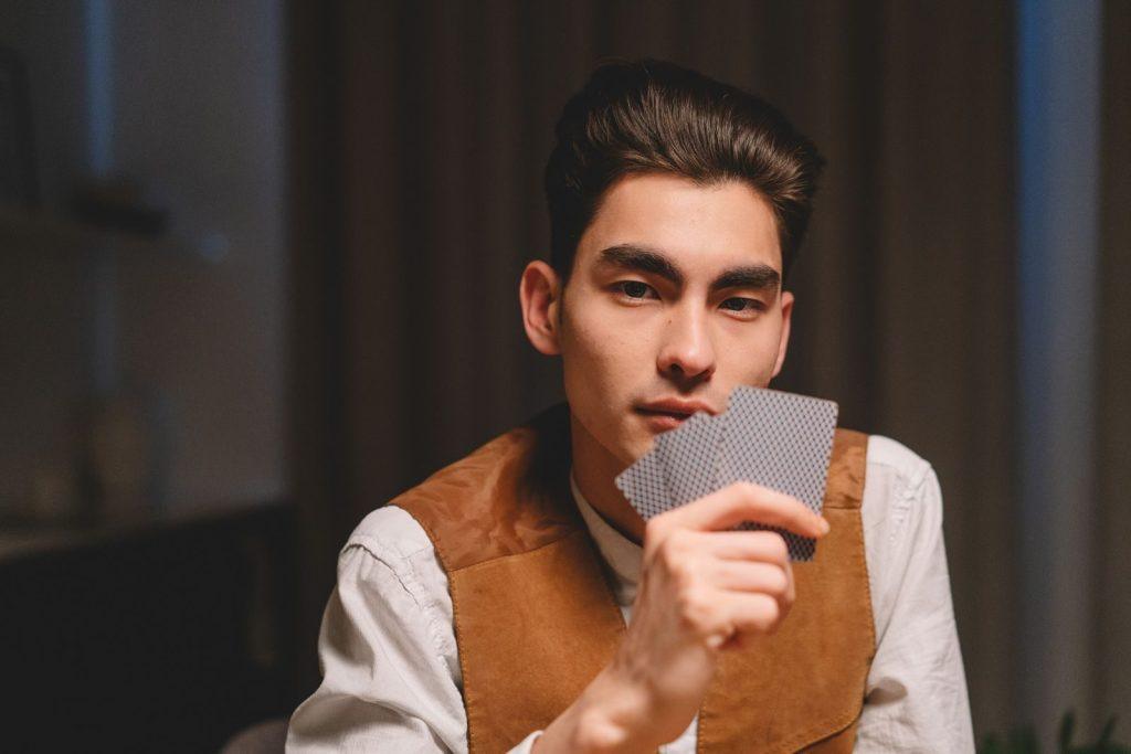 Serious Asian man with poker face holding cards, indoors.